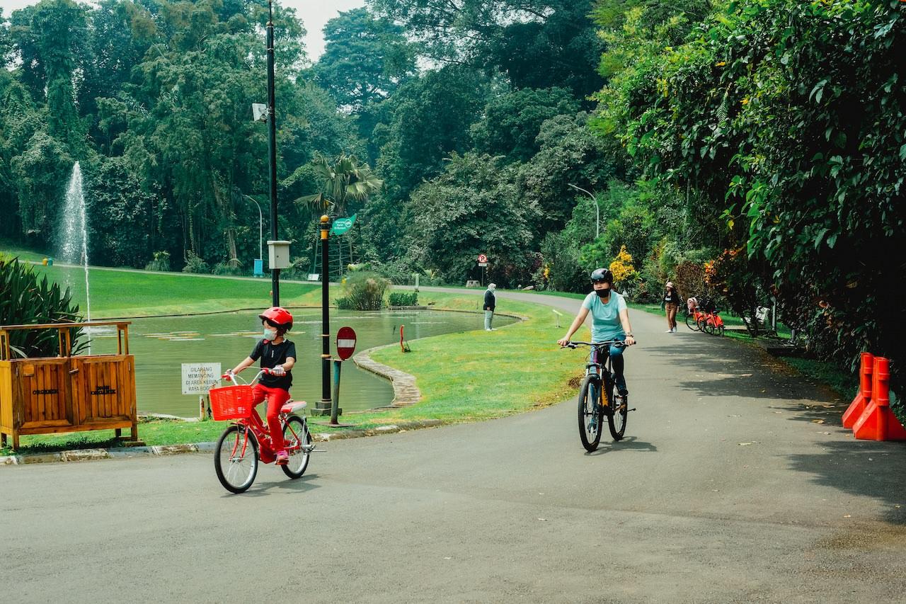 Bogor, Indonesia - March 6, 2021: People cycling wearing masks while on vacation at Bogor Botanical Gardens during Covid-19 pandemic